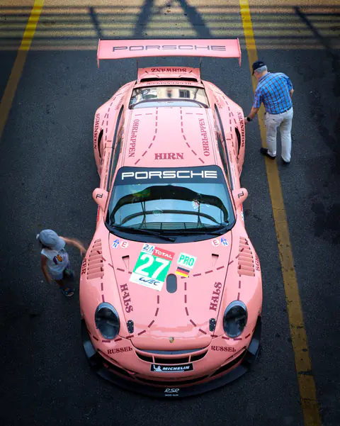 Porsche 911 RSR con livrea rosa fotografata dall'alto in pit lane con i meccanici