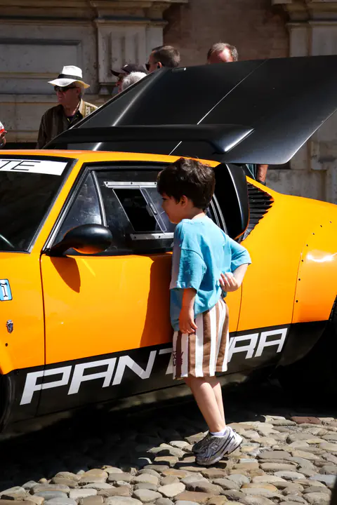 Un bambino osserva una De Tomaso Pantera arancione parcheggiata su un selciato